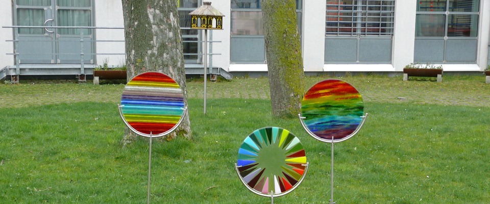 Glasartikel der Arbeitstherapie, Sonnenfänger auf Edelstahlständer, im Hintergrund: Futterhaus auf Edelstahlsäule